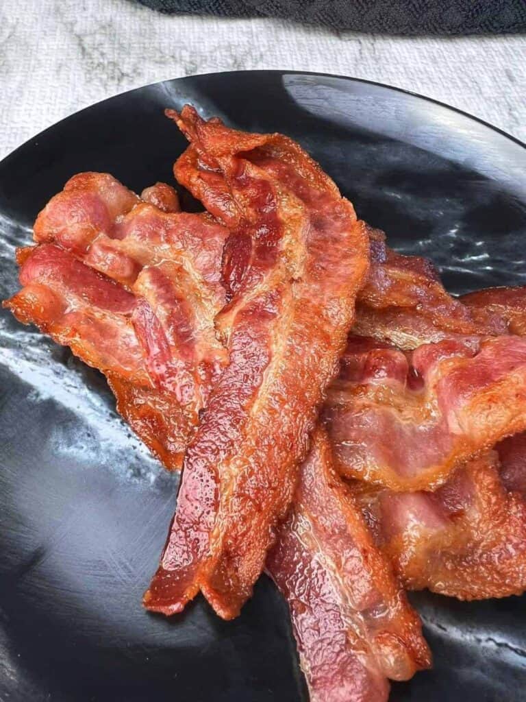 cooked bacon served on a black plate.