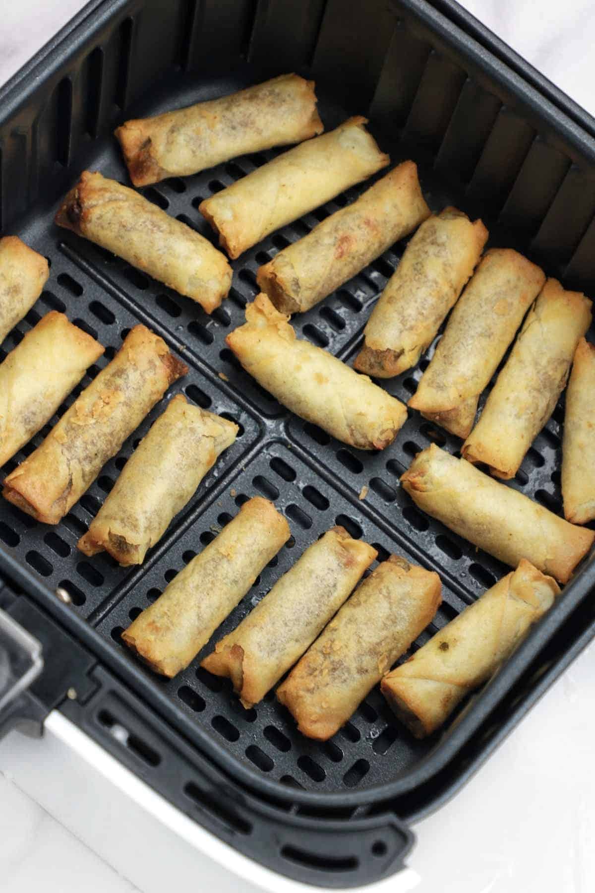 cooked frozen spring rolls in air fryer basket.