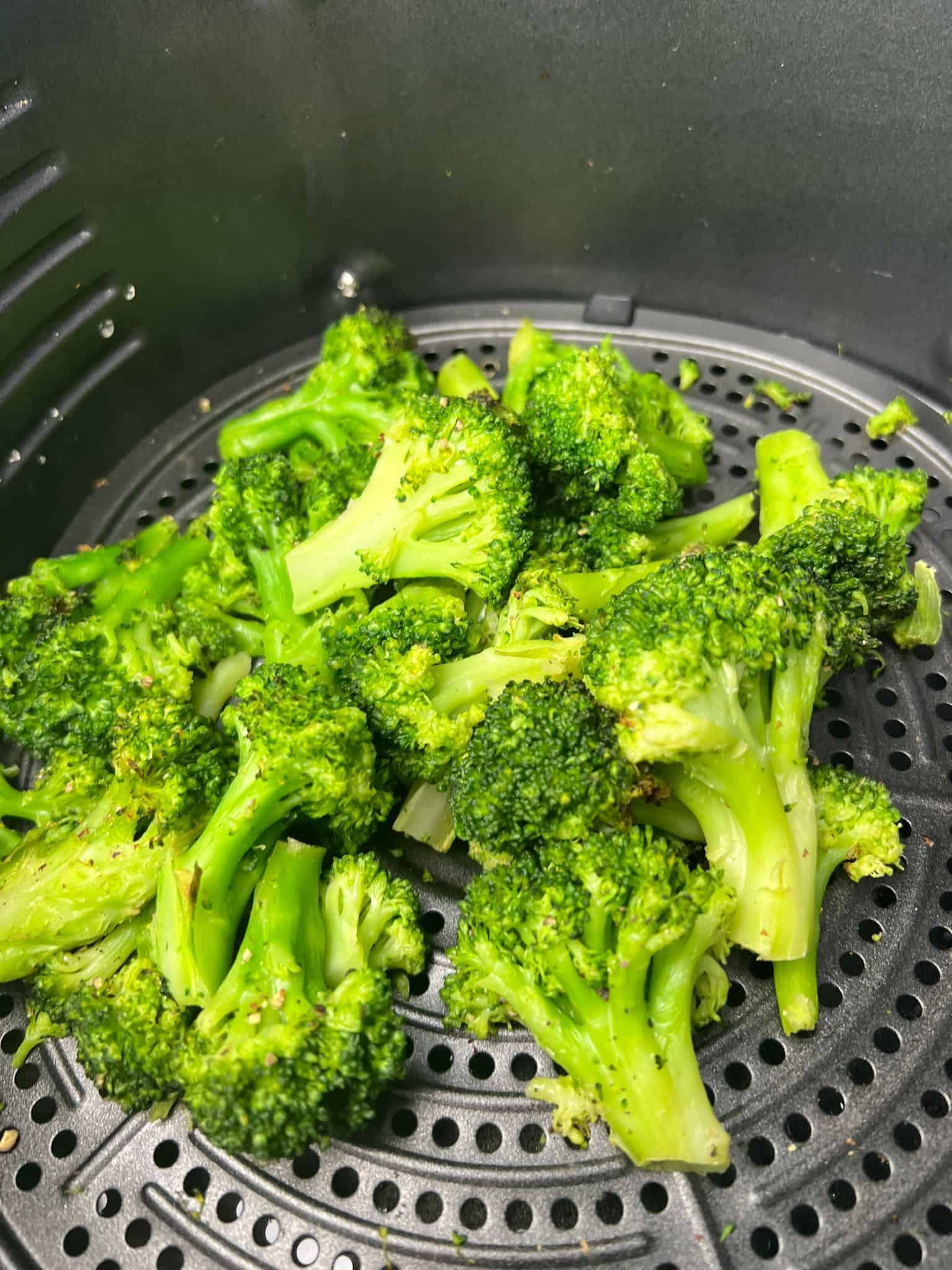 cooked frozen broccoli in air fryer basket.